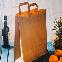 Hohe Einkaufstüte aus Kraftpapier braun neben Weinflasche, Ananas und Orangen vor heller Wand