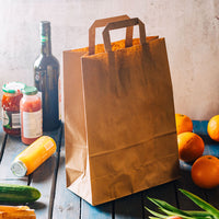 Einkaufstüte aus Kraftpapier braun mit Flaschen, Gläsern, Gurke und Orangen auf Holztisch