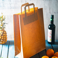 Einkaufstüte aus Kraftpapier braun neben Ananas, Weinflasche und Orangen auf blauem Holztisch